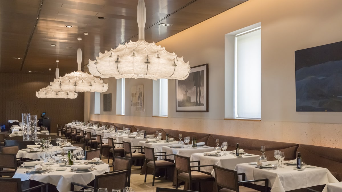 Interior dining room of the Parador with white-dressed tables and large hanging white lamps.