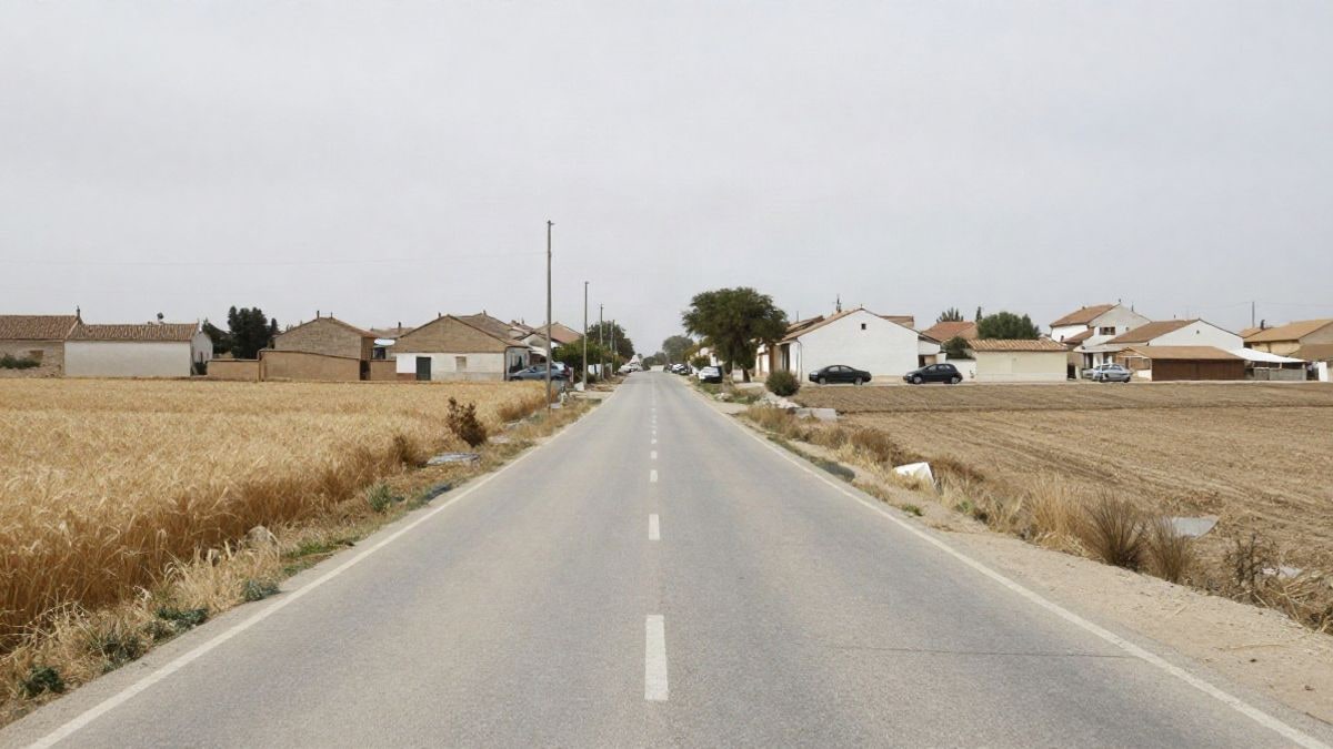 Imagen ilustrativa: camino rural que converge hacia las primeras casas de un pueblo, con campos de cereal a los lados y cielo nublado
