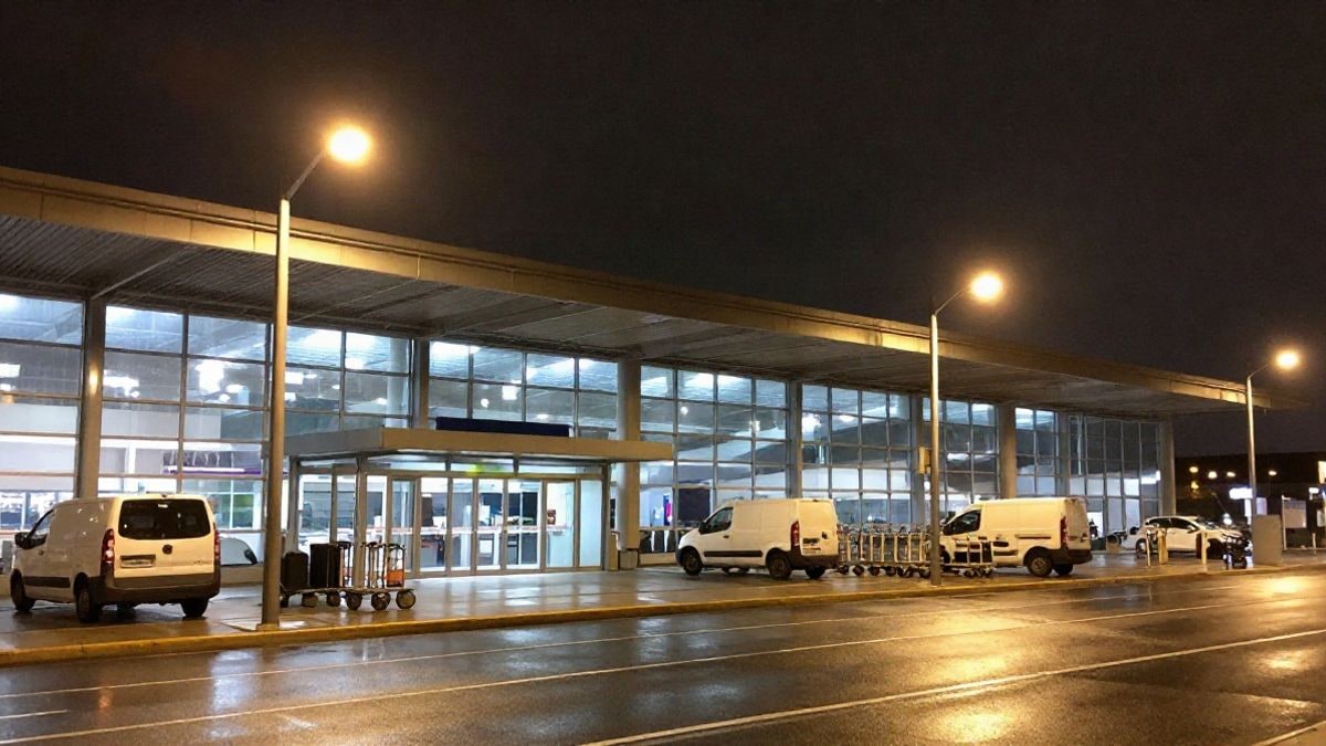 Imagen ilustrativa: fachada de una terminal aeroportuaria de noche con luces artificiales y carros de equipaje