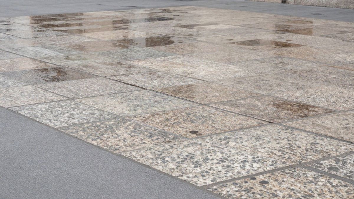 Imagen ilustrativa: detalle de adoquines de granito gastados en una plaza urbana con el suelo húmedo