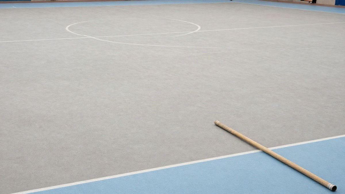 Illustrative image: floor of an empty sports hall with a wooden staff on a light mat