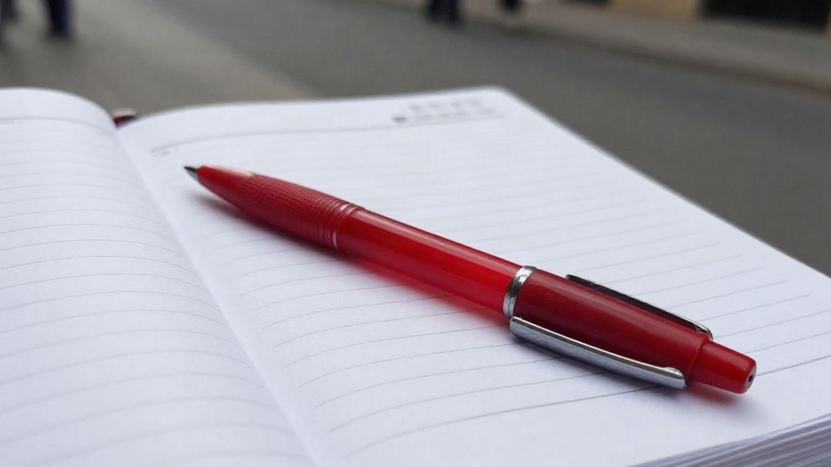 Imagen ilustrativa: bolígrafo rojo sobre una agenda de papel abierta con las páginas en blanco
