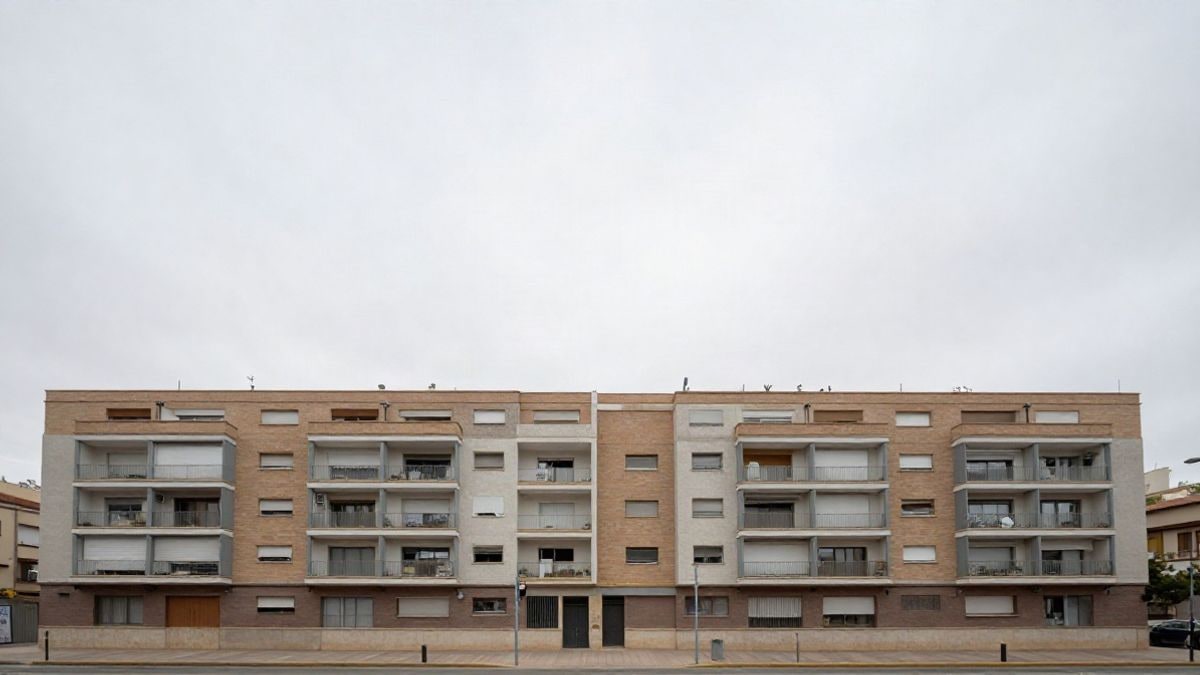 Illustrative image: facade of a residential block viewed from the street, small and off-centre, under a cloudy and clear sky