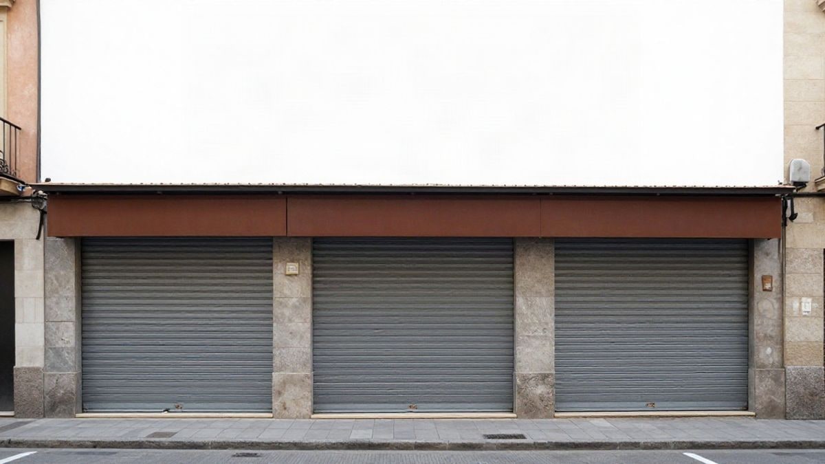 Imagen ilustrativa: fachada de local comercial con persiana metálica cerrada en una calle tranquila de una ciudad española