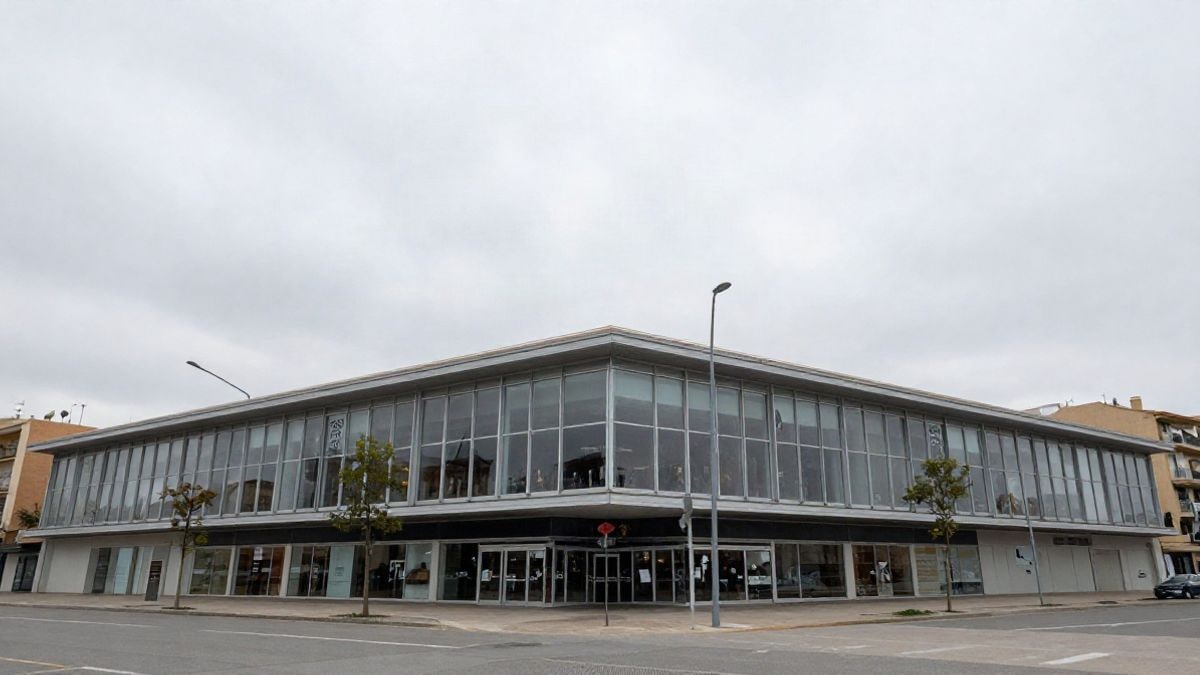 Illustrative image: glass-fronted facade of a modern shopping centre viewed from the ground, with a cloudy sky in the background