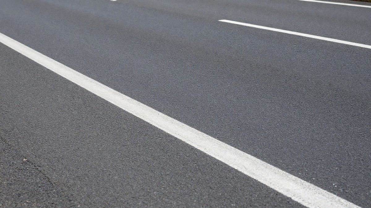 Illustrative image: detail of dark asphalt with white road markings on a road leading to a large city