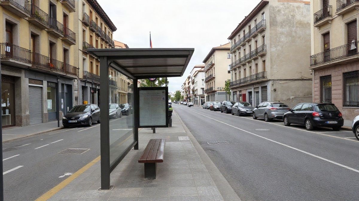 Imagen ilustrativa: avenida urbana amplia con una parada de autobús vacía y fachadas corrientes bajo cielo nublado