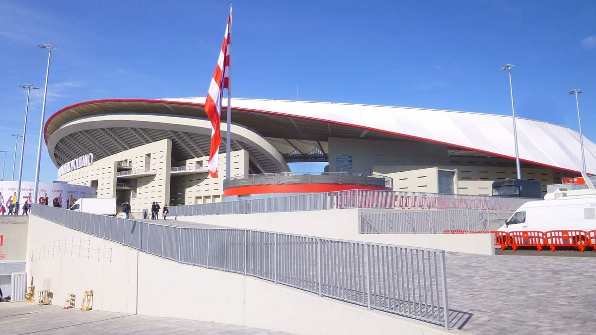 Fachada exterior del Estadio Metropolitano con bandera rojiblanca y vallas junto a la explanada