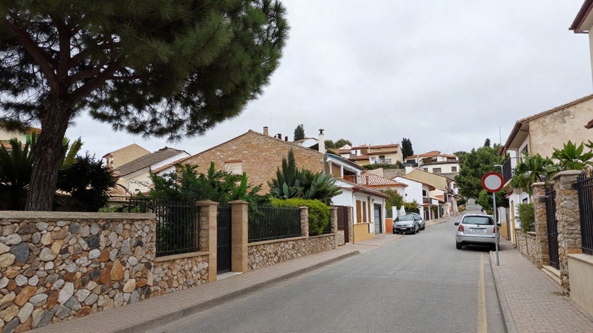 Illustrative image: residential street on a slope with pines and stone walls in a mountain municipality