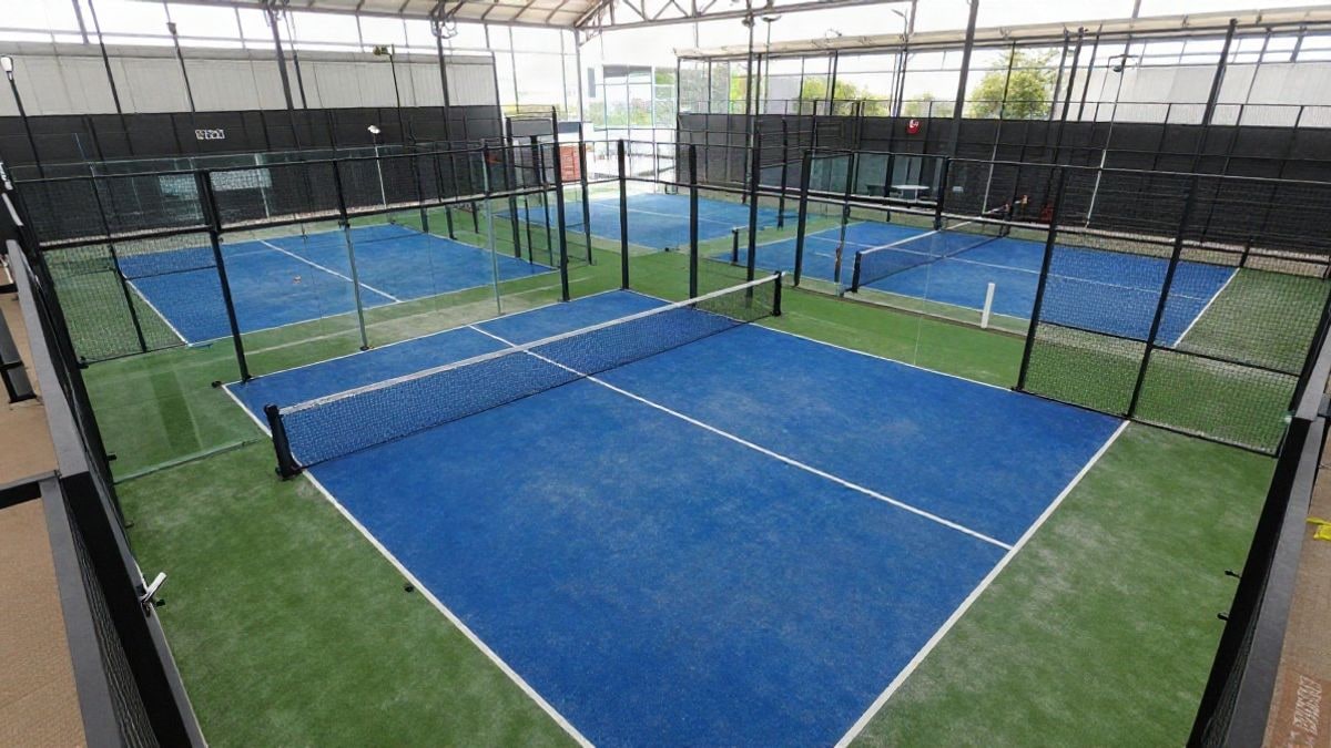 Illustrative image: an empty padel court viewed from above, with the net and side glass, in an indoor arena with natural light.